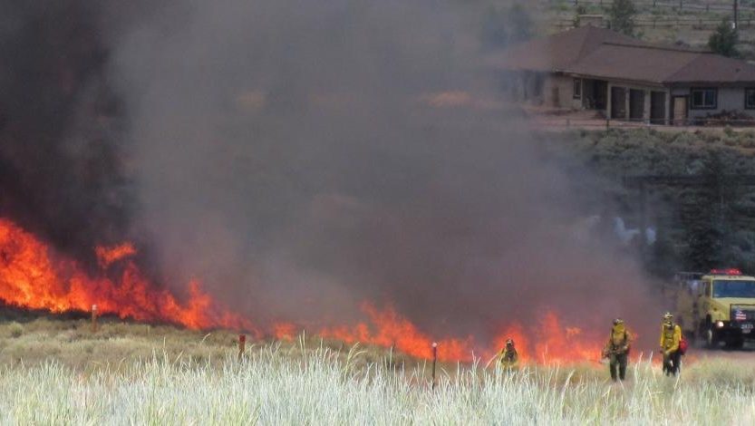 Firefighters responding to a wildfire with flames and smoke in the background.